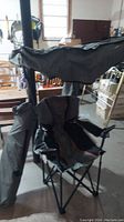 Photo of one Fair Wind folding camp chair with built-on awning and carrying bag standing upright in a garage setting.