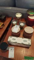 Nine assorted candles in various styles of glass and wooden jars placed on wooden table.