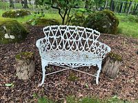 Front view of white cast metal loveseat bench showing intricate scrollwork, weathering, and peeling paint.