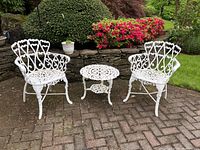 Photo showing the full set of white cast metal outdoor furniture including two armchairs and one round side table in a garden setting.