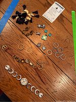 Photo showing nine rings in silver and gold tones, some with stones, a brown leather strap bracelet with decorative gold-tone and stone accents, a DKNY silver-tone watch with circular links, and several earrings and pendants.