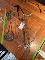 Photo of eight different costume jewelry necklaces arranged on wooden floor showing various styles, beads, chains, and pendants.