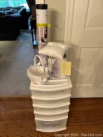 View of stacked white plastic craft bin with five drawers topped by rolled diffuser poster, white satin flower girl basket, and two white satin pillows.