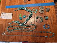 Full view of assorted jewelry pieces laid on wood surface showing necklaces, earrings, rings, and bracelets