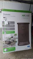 Photo of the original box showing the Aircare Essickair Pedestal Evaporative Humidifier with features including max output 88 pints, up to 9 gallons output per 24 hours, 3.5 gallon tank capacity, and remote control model #1999.