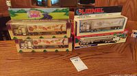 Four boxed semi trucks arranged side by side on a wooden surface, including two Dunkin' Donuts semi trucks and two Lionel Mobil trucks in original packaging.
