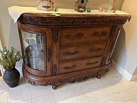 Front view of wooden server showing curved glass display doors and three drawers with ornate handles, detailed carvings along top edge and base.
