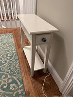 Side view of white side table showing drawer with blue ceramic knob and bottom shelf.