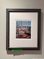 Full view of the framed artwork hung on a wall with a dark gray textured frame and cream matting.