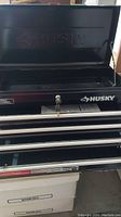 Front view of Husky tool chest with key in lock, showing the top pull-down compartment open and lower four drawers.
