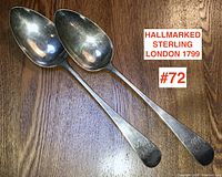 Pair of Georgian sterling silver serving spoons with London hallmark 1799 laid side by side on wooden surface.