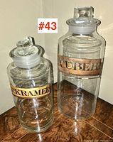 Two Victorian blown glass apothecary bottles with glass stoppers and paper labels 'DR. KRAMER' and 'CUBEB' placed side by side on wooden surface.