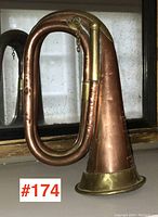 Side view of antique copper and brass bugle showing the coiled tubing, bell, and some dents.