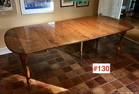 Angled side view of the antique wooden dining table fully extended with four leaves in place on tiled floor, showing rounded ends and turned legs.