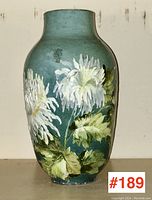 Front view of vase showing two large white chrysanthemum blooms and foliage against teal ground