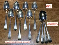 Lot of eleven Georgian and Victorian sterling silver tea spoons laid out on a wooden surface, including a group of four Glasgow 1848 spoons with beaded edges and seven others with engraved handles and worn hallmarks.
