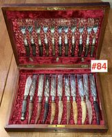 Open wooden box showing the full set of 12 knives and 12 forks arranged in red velvet lining.