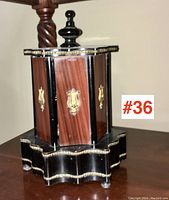 Front view of the antique holder showing black base with gold trim and wood veneered panels with brass accents.