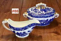 Photo of small tureen with lid and matching gravy boat with Blue Willow pattern and gold accents on wood table