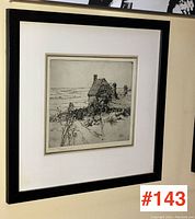 Framed signed black and white print of a rural cottage and landscape, hanging on wall, with a black frame and white mat.