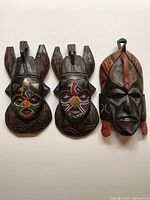 Three African masks displayed side by side showing intricate beadwork and carved wood details.