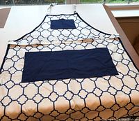 White apron with geometric blue trellis pattern and blue pockets laid flat on a light-colored surface.