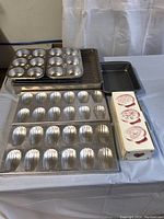 Overview of bakeware items including muffin tins, cooling rack, half sheet pan, madeleine molds, cookie stamp, and small baking pan.