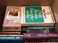 Stack of assorted hardcover and paperback books including The New Child Health Encyclopedia and Old-Fashioned Cures and Proven Home Remedies.