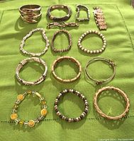 Lot of assorted bracelets laid out on green cloth showing variety of styles including metal, beaded, and rhinestones