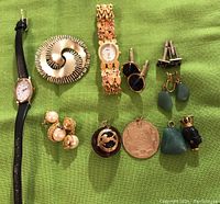 Photo showing full collection of costume jewelry items including 2 watches, multiple earrings, cufflinks, pendants and a pin laid out on green fabric.