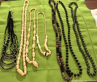 Seven assorted beaded necklaces laid out on a green textile, showing variety in bead size, shape and color.