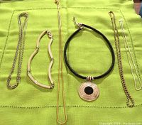 Full view of 5 assorted necklaces on green fabric background.