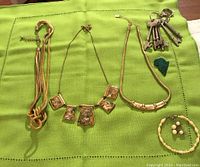 Lot laid out on a green cloth background, showing four gold-tone necklaces, a freshwater pearl bracelet with matching pearl earrings, a green carved pendant, and a set of vintage skeleton keys on a keyring.