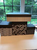 Four decorative storage boxes stacked and side by side on a white surface against window background.