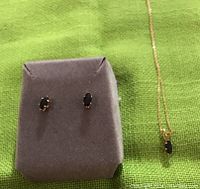 Full view of the pair of gemstone earrings and matching necklace on green fabric background.