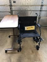 Black transporter chair shown with adjustable table behind it; heating pad placed on chair seat.