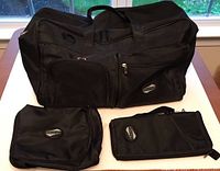 Photo showing the American Tourister 22 inch black weekender bag with the passport and toiletries cases placed in front of it on a table.