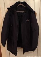 Front view of men's black quilted jacket by The North Face with hood, size 3X, unzipped showing lining
