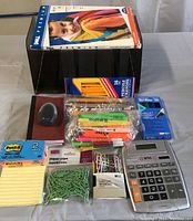 Display of all small office items including notebooks, pencils, highlighters, paper clips, post-it notes, pencil sharpener, calculator, and marker pack.
