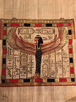 Photo of a hand-painted papyrus art depicting Egyptian Goddess Isis with outstretched wings and surrounding hieroglyphics, framed with red and black accents.