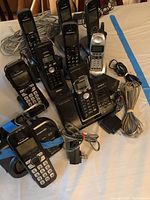 Photo showing 6 Panasonic corded phones with numeric keypads, LCD displays, power cords, and bases on a table.