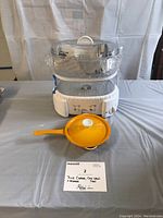 Full view of Oster steamer stacked with two steaming trays and yellow cast iron pan with lid on table