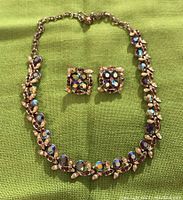 Full view of necklace and earrings on green fabric background showing stones and leaf detail.