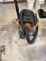 Front-top angled view of Ridgid 12 gallon wet/dry vacuum showing hose, nozzle attachments, and motor housing details.