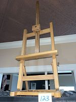 Front view of wooden adjustable tabletop artist easel showing central vertical support with adjustable holder and horizontal shelf for artwork.