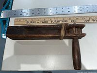 Photo of wooden hand-cranked gas alarm placed next to rulers to show size and condition. Handle and body structure with tied string visible.