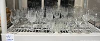 Wide shot of the shelf showing the full set of clear lead crystal glasses including wine and cordial glasses arranged in rows.