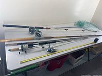 Full view of five fishing rods with reels and one fishing net on table, including measuring tape for scale