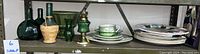 Green glass bottles, Old Country Shop dishes, oil lamp, and decorative plates on shelf