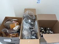 Photo showing three boxes filled with assorted metal jewelry pieces, some in plastic and paper bags, including bangles and bracelets